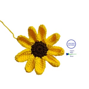 May include: A crocheted sunflower with yellow petals and a brown center. The sunflower is on a white background. The text "Crochet Pattern Gigi's Blue Rose" is in a circle on the right side of the image.