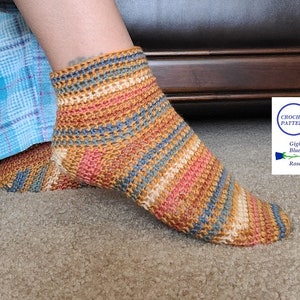 Könnte beinhalten: Ein Paar gestreifte Häkelsocken in den Farben Braun, Blau, Creme und Rosa. Die Socken werden an den Füßen einer Person gezeigt. Das Bild enthält den Text "Crochet Pattern Gigi's Blue Rose".