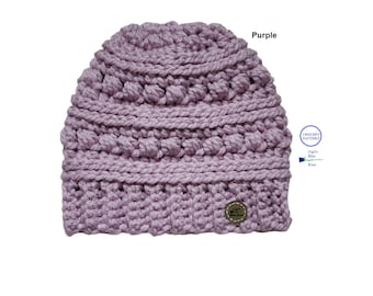May include: Purple crochet beanie hat with a textured stitch pattern. The hat has a small brown label with the text "Gigi's Blue Rose" on it.