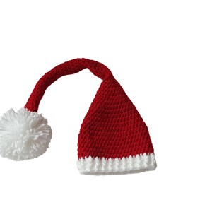 May include: A red and white crocheted Santa hat with a white pom-pom and a long, curved tip. The hat is primarily red with a white brim and pom-pom, perfect for holiday celebrations.