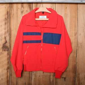 May include: Red jacket with blue stripes and a zip closure. The jacket has a stand-up collar and long sleeves. The brand name "Sherpa" is visible on the label.