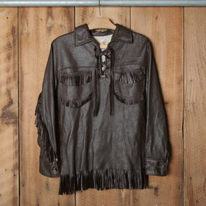 May include: A brown leather jacket with fringe detailing and a lace-up front. The jacket has long sleeves and a collar.