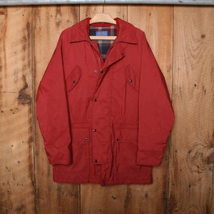 Op de afbeelding: Een rood, lang mouwig jack met een geruite voering. Het jack heeft een ritssluiting en knoopsluiting, twee klepzakken op de borst en twee lagere zakken.