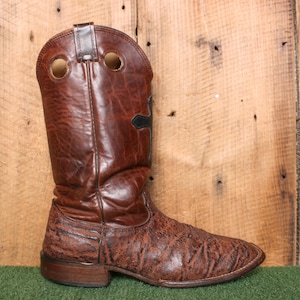 May include: A brown leather cowboy boot with a textured pattern and a black cross design on the side.