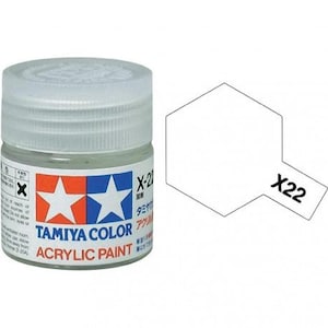 May include: A jar of Tamiya Color acrylic paint, labeled X-22, with a white, semi-transparent appearance. The label features a red and blue design with white stars and the text "Tamiya Color Acrylic Paint". A white paint swatch is next to the jar.