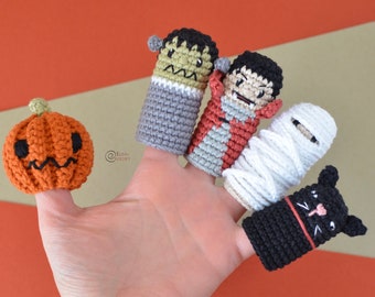 Könnte beinhalten: Fünf gehäkelte Fingerpuppen, darunter ein Kürbis, Frankenstein, ein Vampir, eine Mumie und eine schwarze Katze. Die Puppen befinden sich auf einer Hand und sind bereit zum Spielen.