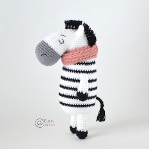 May include: A crocheted zebra toy with black and white stripes, wearing a pink scarf. The zebra has a black mane and tail.