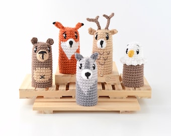 Könnte beinhalten: Fünf gehäkelte Fingerpuppen, die Waldtiere darstellen: ein Fuchs, ein Reh, ein Bär, ein Wolf und eine Eule. Die Puppen sind auf einer Holzplattform angeordnet.