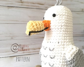 May include: A crocheted seagull amigurumi toy with a white body, gray wings, and a yellow and orange beak. The toy is sitting on a wooden surface.