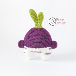 May include: A purple and white crocheted turnip plush toy with a green leafy top. The toy has a smiling face with black eyes and a black mouth.