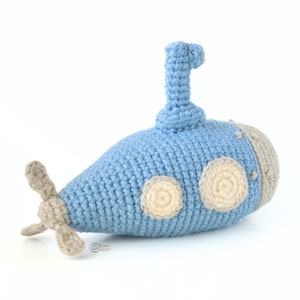 May include: A crocheted blue submarine toy with a gray propeller and beige portholes.