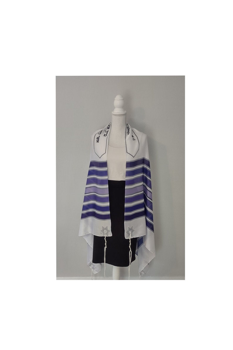 Op de afbeelding: Witte tallit met blauwe strepen en een Davidster-ontwerp. De tallit heeft Hebreeuwse tekst op de franjes.