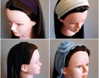 Op de afbeelding: Een collectie van vier haarbanden getoond op etalagepoppen. De set bevat een effen donkerpaarse haarband, een geplooide off-white haarband, een eenvoudige zwarte haarband en een lichtblauwe haarband met een grote stoffen roos als accent.