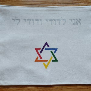 Op de afbeelding: Witte canvas tas met een ritssluiting. De tas heeft een regenboogkleurige Davidster en de Hebreeuwse tekst "Ani L'dodi V'dodi Li" in zilveren borduurwerk.
