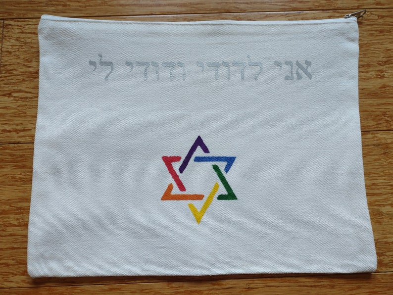 Op de afbeelding: Witte canvas tas met een ritssluiting. De tas heeft een regenboogkleurige Davidster en de Hebreeuwse tekst "Ani L'dodi V'dodi Li" in zilveren borduurwerk.