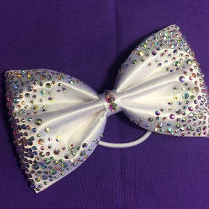May include: A white satin bow with iridescent rhinestones, attached to a black elastic band.