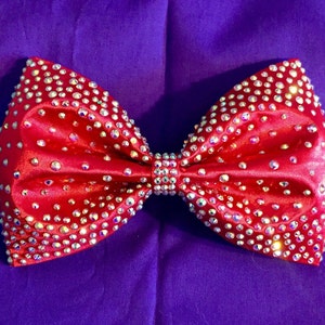 May include: A large red satin bow with a center piece of rhinestones. The bow is decorated with small, clear rhinestones.