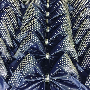 May include: A close-up of multiple navy blue satin bows decorated with silver rhinestones. The bows are arranged in rows and are all the same size.