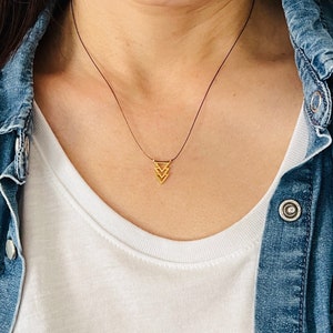May include: A gold triangle pendant necklace on a black cord. The pendant is made of three stacked triangles.