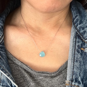 May include: A delicate silver chain necklace with a light blue teardrop-shaped gemstone pendant.