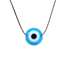May include: A blue evil eye charm necklace on a brown cord. The charm is round and has a white circle with a black pupil in the center.