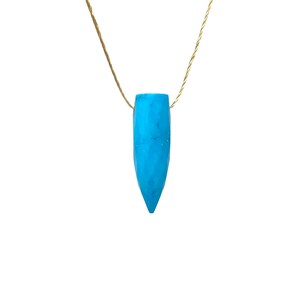 May include: A turquoise blue gemstone pendant on a gold chain. The pendant is shaped like a teardrop and has a smooth, polished finish.