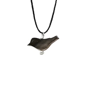 May include: A silver bird pendant necklace with a black cord. The bird is in flight and has a small white bead at the bottom.