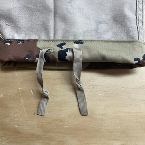 May include: Close-up of a pair of tan drawstrings attached to a camouflage fabric waistband. The drawstrings are tied in a knot.