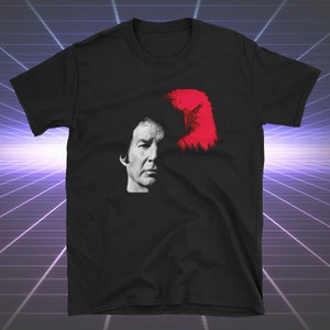 May include: Black t-shirt with a graphic of a man's face with a red eagle superimposed over his head.