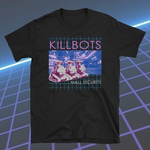 May include: Black t-shirt featuring a retro graphic design. The design includes the word "KILLBOTS" in pink, above an image of three robot-like figures. Below the image, the text reads "MALL SECURITY."