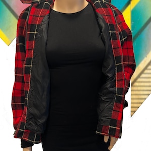 May include: A red and black plaid jacket with a zipper closure. The jacket has a black lining and gold trim.