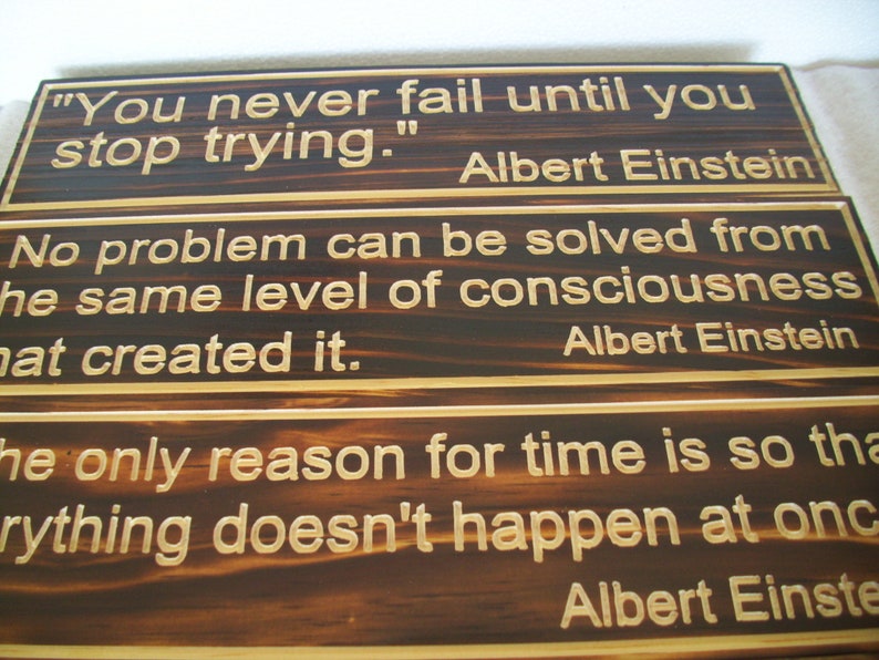 May include: Wooden plaques with quotes by Albert Einstein. The top plaque reads "You never fail until you stop trying." The middle plaque says "No problem can be solved from the same level of consciousness that created it."