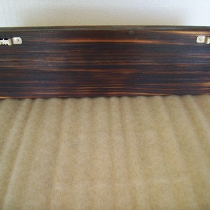 May include: A dark brown, rectangular wooden shelf with a distressed finish. Two metal sawtooth hangers are attached to the back for wall mounting. The wood grain is visible.