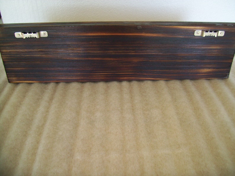 May include: A dark brown, rectangular wooden shelf with a distressed finish. Two metal sawtooth hangers are attached to the back for wall mounting. The wood grain is visible.