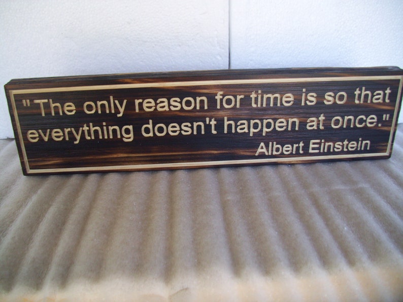 May include: A rectangular wooden sign with a dark brown finish and a lighter border. The sign features the quote "The only reason for time is so that everything doesn't happen at once." by Albert Einstein, engraved in a light color.