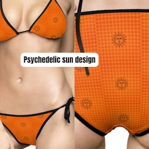 Könnte beinhalten: Oranges Bikini-Set mit psychedelischem Sonnendesign. Das Bikini-Oberteil ist im Dreiecksstil mit schwarzem Besatz gehalten, und die Unterteile sind klassisch geschnitten mit Bindebändern. Der Stoff zeigt ein sich wiederholendes Muster aus lächelnden Sonnen.