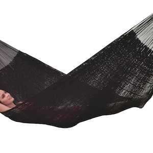 May include: A black hammock with a person lying in it. The hammock is made of a woven material and has a slight sheen.