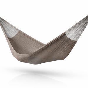 Può includere: Un'amaca marrone sospesa a mezz'aria su sfondo bianco. L'amaca è realizzata in tessuto intrecciato con estremità bianche e legacci in corda nera. Progettata per il relax e l'uso all'aperto.