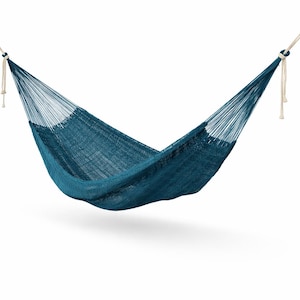 May include: A teal-colored hammock suspended against a white background. The hammock is made of woven material and hangs from white rope attachments. The hammock is designed for relaxation and outdoor use.
