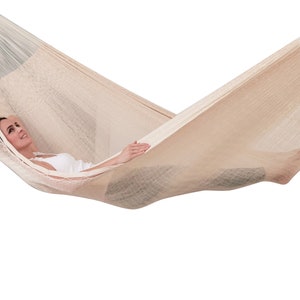 Puede incluir: Una persona relajándose en una hamaca beige. La hamaca está hecha de un material tejido y tiene un aspecto natural y rústico.