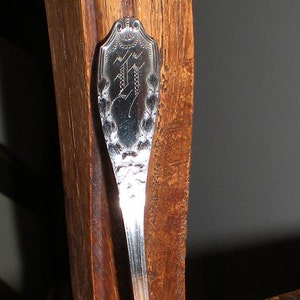May include: A silver serving spoon with an ornate handle and a bowl with a scalloped edge. The spoon is resting on a wooden surface.