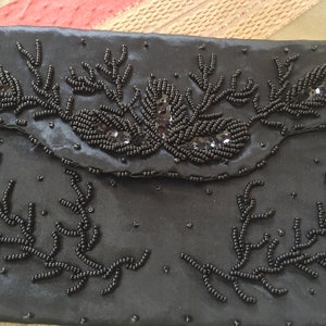 Puede incluir: Un bolso de mano de sat&eacute;n negro con un dise&ntilde;o de cuentas. El bolso est&aacute; decorado con cuentas negras y lentejuelas en un patr&oacute;n floral.