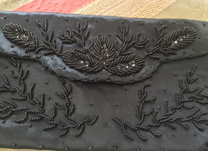 Puede incluir: Un bolso de mano de sat&eacute;n negro con un dise&ntilde;o de cuentas. El bolso est&aacute; decorado con cuentas negras y lentejuelas en un patr&oacute;n floral.
