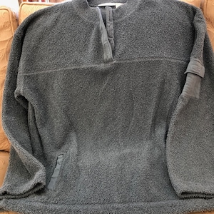 May include: A dark gray fleece pullover with a buttoned neck and a patch on the sleeve.