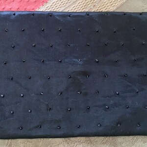 Puede incluir: Un bolso de noche negro con cuentas, con una textura lisa y satinada. El bolso est&aacute; adornado con peque&ntilde;as cuentas negras que est&aacute;n espaciadas uniformemente por toda la superficie.