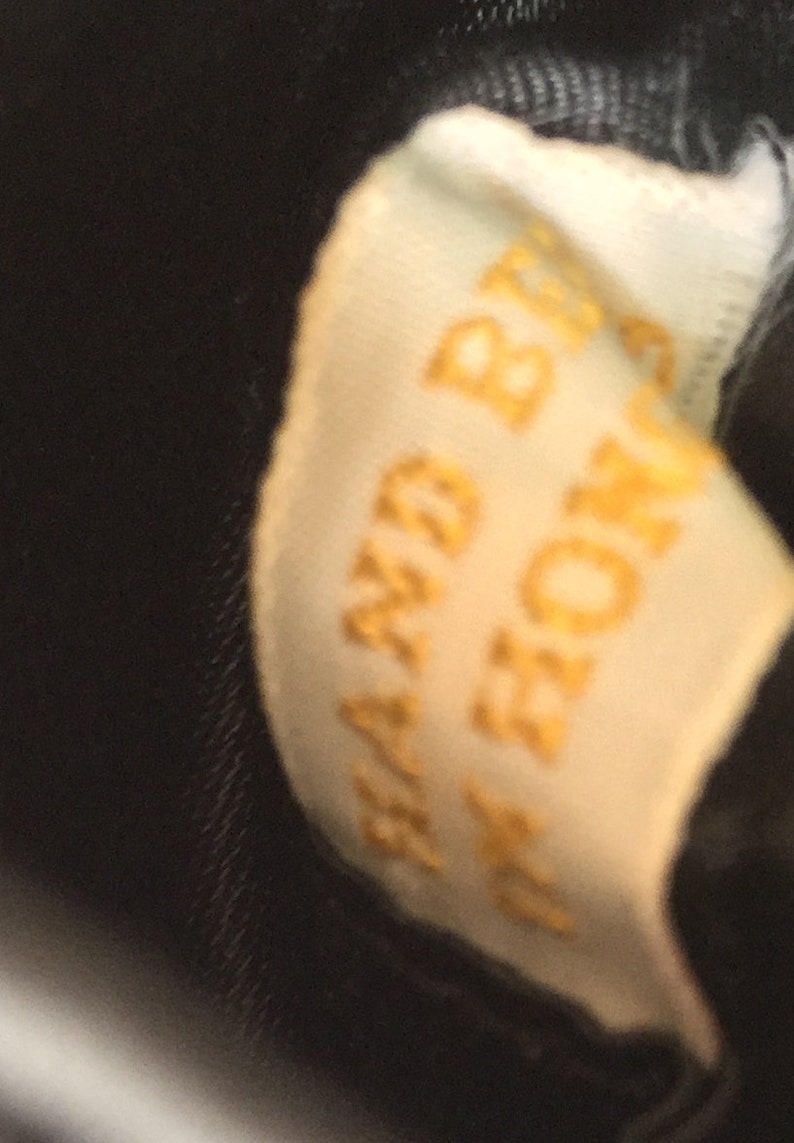 Puede incluir: Primer plano de una etiqueta blanca con el texto "HAND BAGS" en letras doradas.