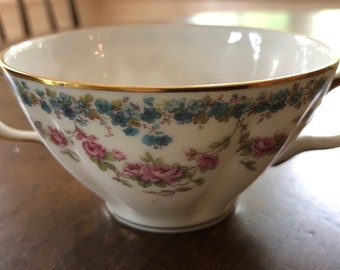 May include: A white porcelain teacup with a gold rim and floral pattern. The cup has two handles and is decorated with pink and blue flowers.
