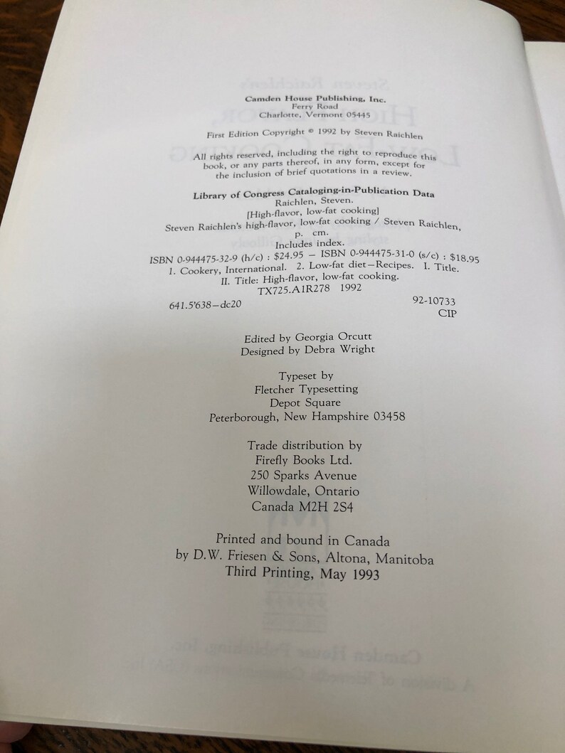 May include: A book cover with the title "High-flavor, Low-fat Cooking" by Steven Raichlen. The cover is white with black text and a black and white illustration of a chef. The book was published in 1992 by Camden House Publishing, Inc.