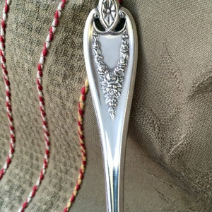 May include: A silver-plated serving spoon with a decorative handle featuring a floral design. The handle is ornate and has a raised design of roses and leaves.