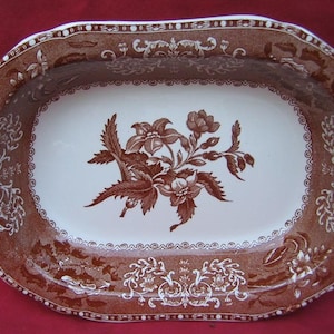 May include: A brown and white oval serving dish with a floral design. The dish has a scalloped edge and a raised rim.